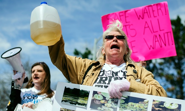 Protesters hold up jugs of discolored water outside the Farmers Market in Flint, marking the one-year anniversary of the city switching from using Detroit water to Flint River water. Photo credit: Sam Owens/AP
