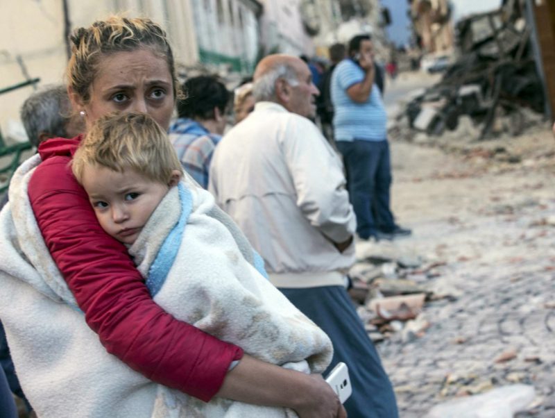 A woman holds a child as they stand in the street following an earthquake, in Amatrice. The magnitude-6 quake was felt across a broad swath of central Italy, including Rome, where residents of the capital felt a long swaying followed by aftershocks. Photo credit: Massimo Percossi/AP