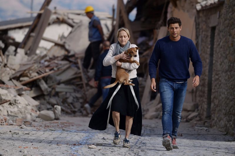 A woman holds a dog in her arms as she walks with a man next to the rubble of buildings in Amatrice. Photo credit: Filippo Monteforte/AFP/Getty